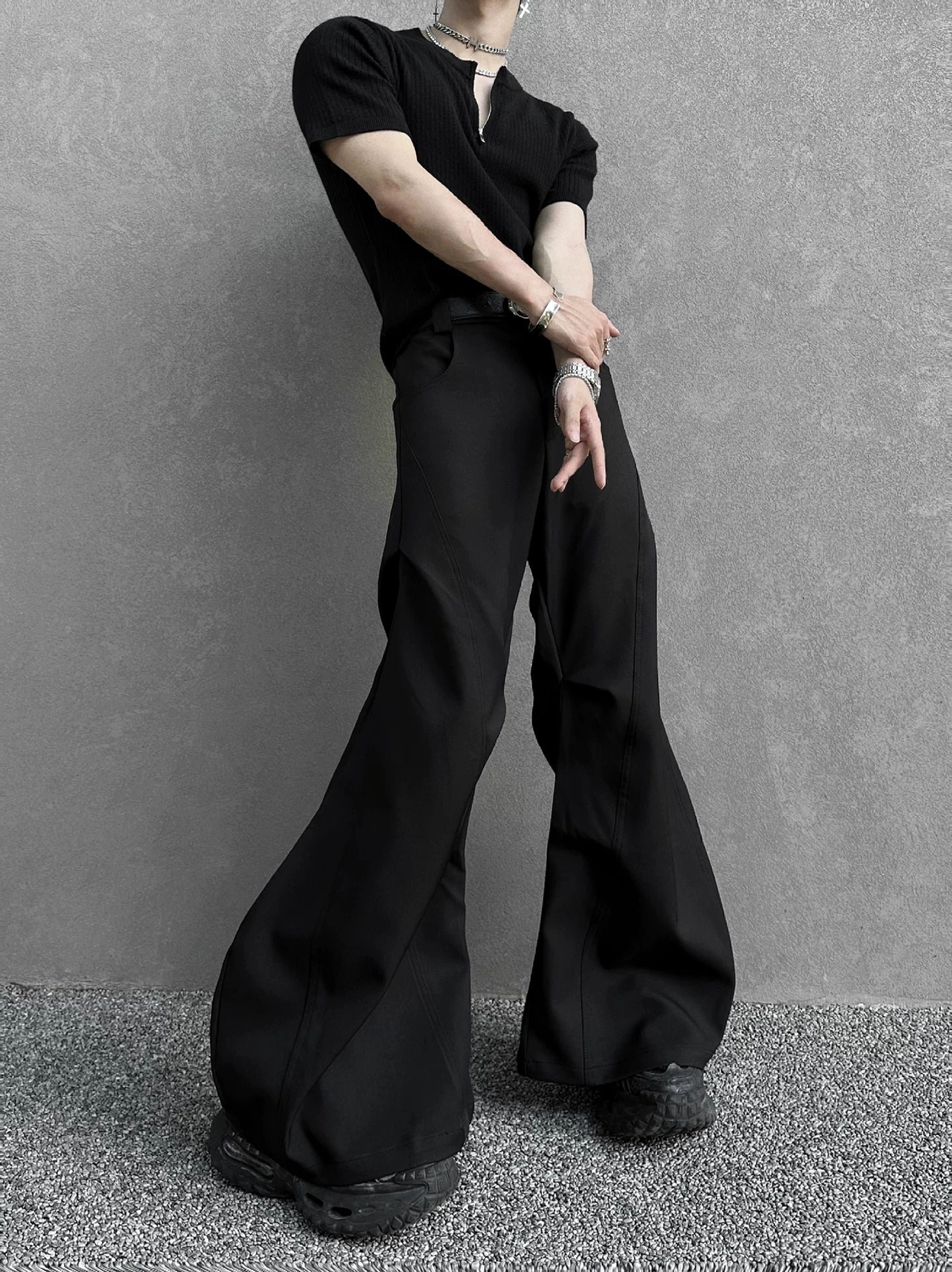 Black hyperwide flare cargo pants shown from a low rear-side angle with a high waist, smooth draped fabric, long floor-skimming hem, black henley top, and chunky shoes