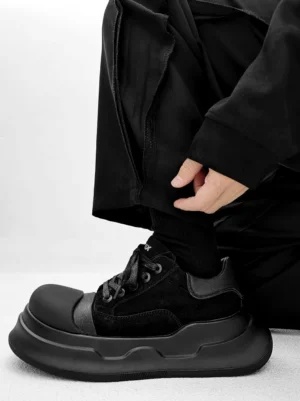 Side profile of black chunky platform sneakers styled with baggy cargo trousers, contrasting upper panels, rounded toe, and elevated sculpted sole