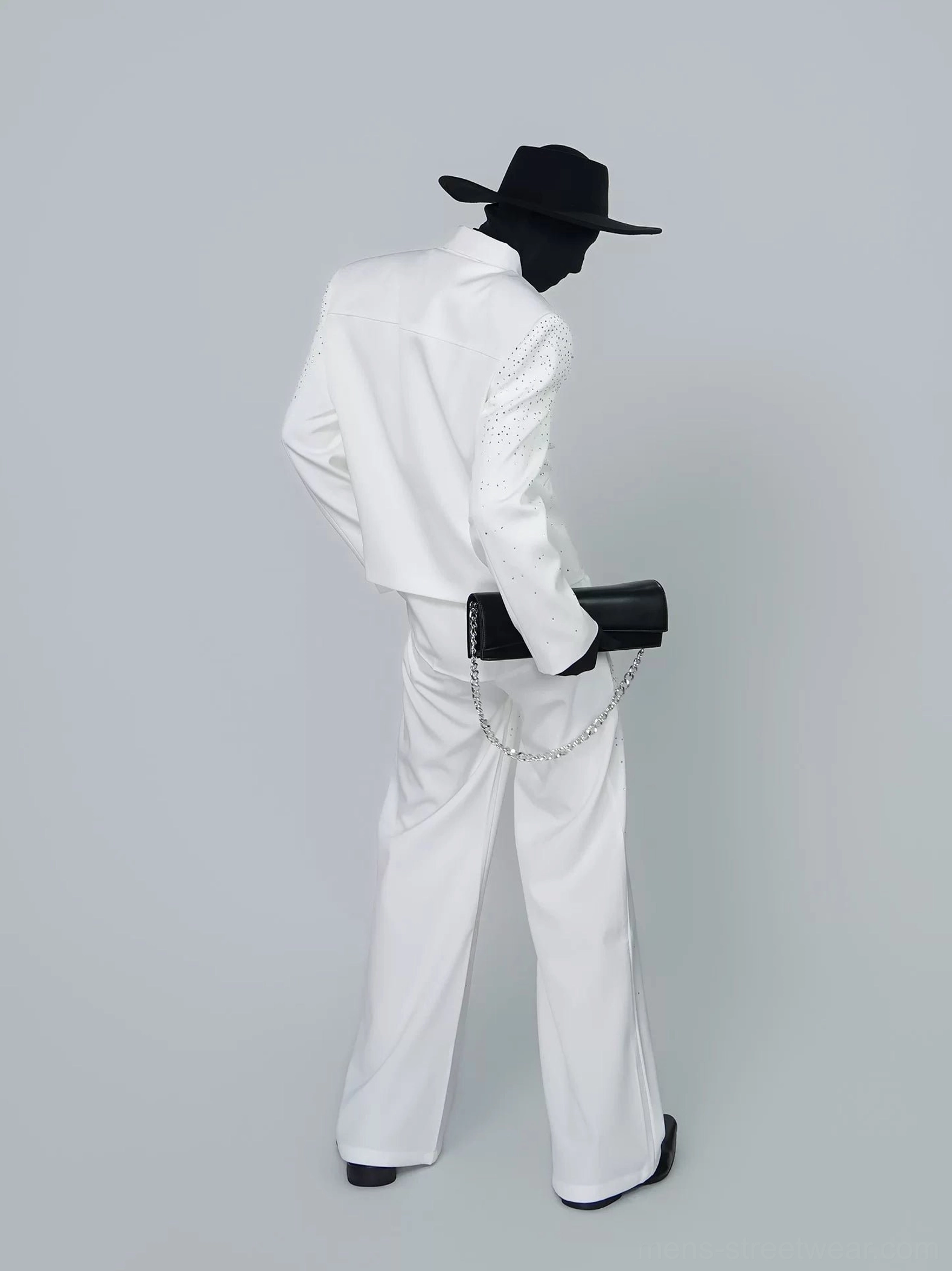 Structured black chain shoulder clutch bag worn from the back with wide-leg trousers and minimalist streetwear styling