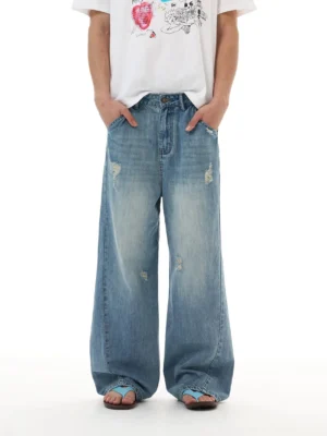 Front full-body view of ocean fade super wide blue jeans with relaxed mid-rise fit, subtle distressed details, and puddled hems styled with a graphic white T-shirt and slides