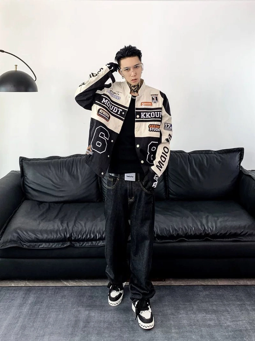 Front view of an off-white and black racing varsity jacket with layered patches, graphic details, dark jeans, and casual sneakers