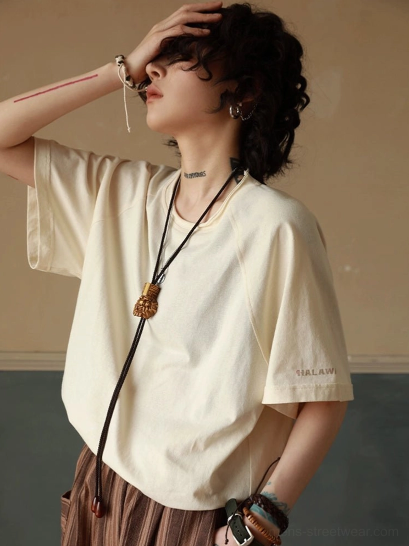 Off-white cotton raglan sleeve T-shirt with relaxed oversized fit, layered bracelets, tassel bag, and striped skirt