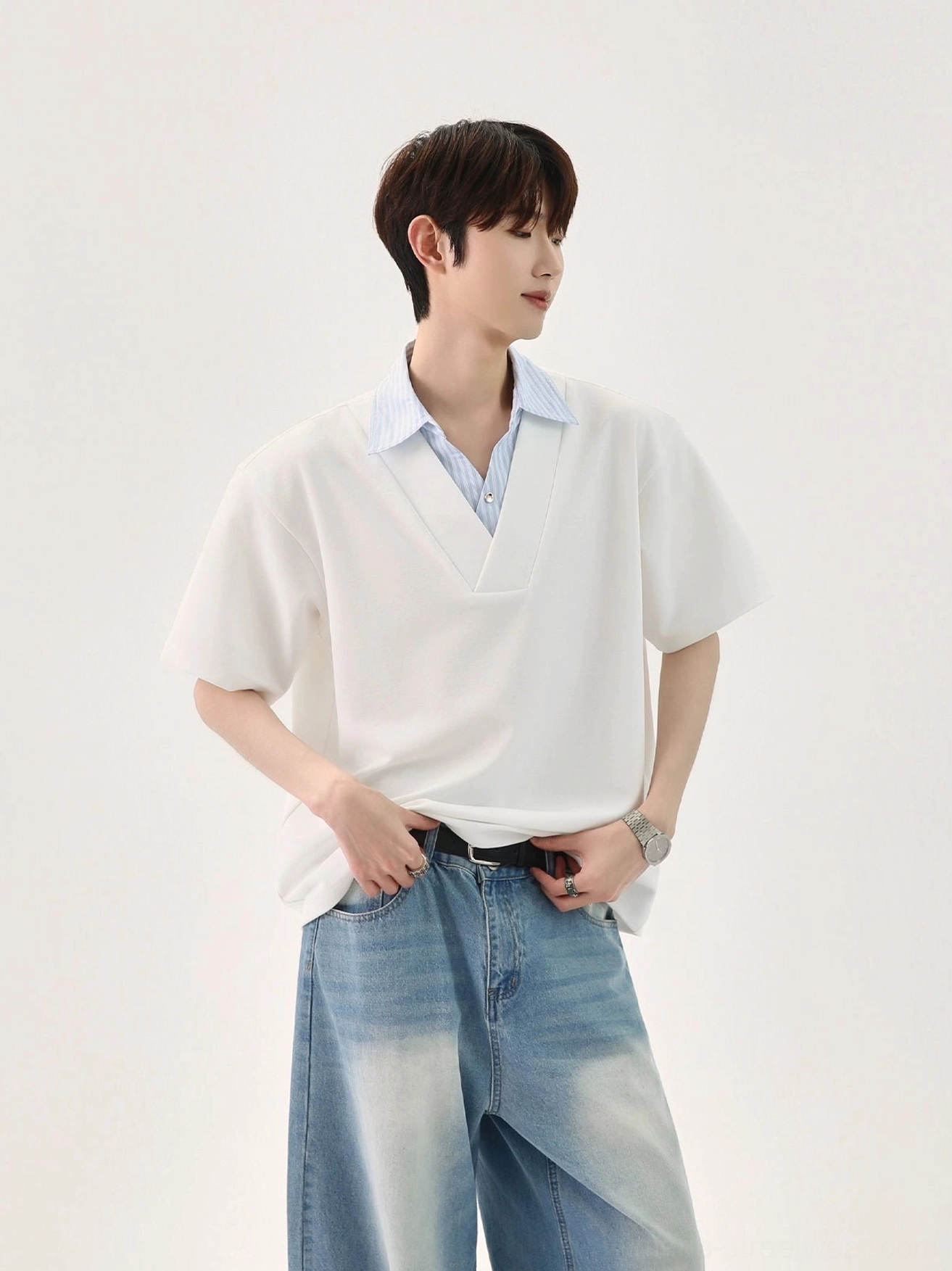 Side view of a relaxed off-white faux layered T-shirt with blue and white striped collar styled with faded blue wide-leg jeans