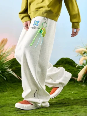 Off-white heather Korean streetwear wide-leg sweatpants shown in motion with floral details, cross embroidery, and tassel pendant
