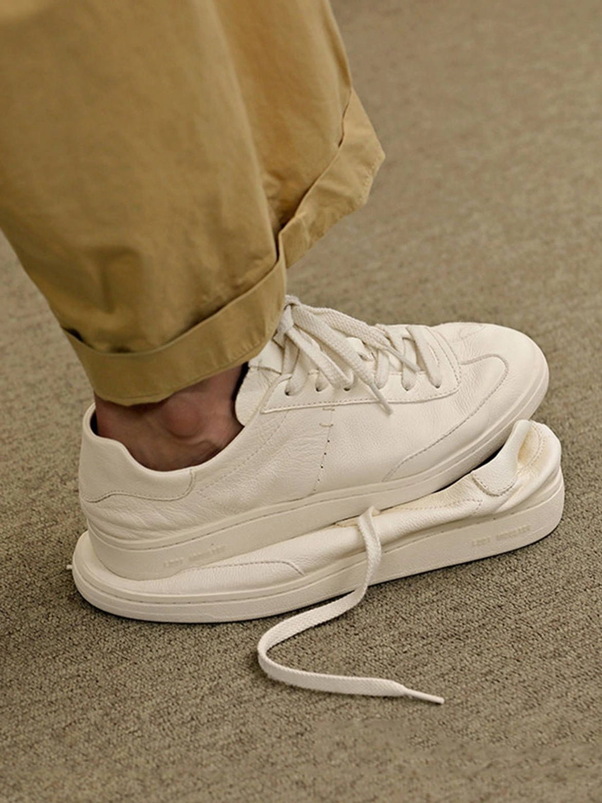 Off-white low-profile leather sneakers worn with cropped khaki trousers, showing the sleek rear profile and casual Korean streetwear fit