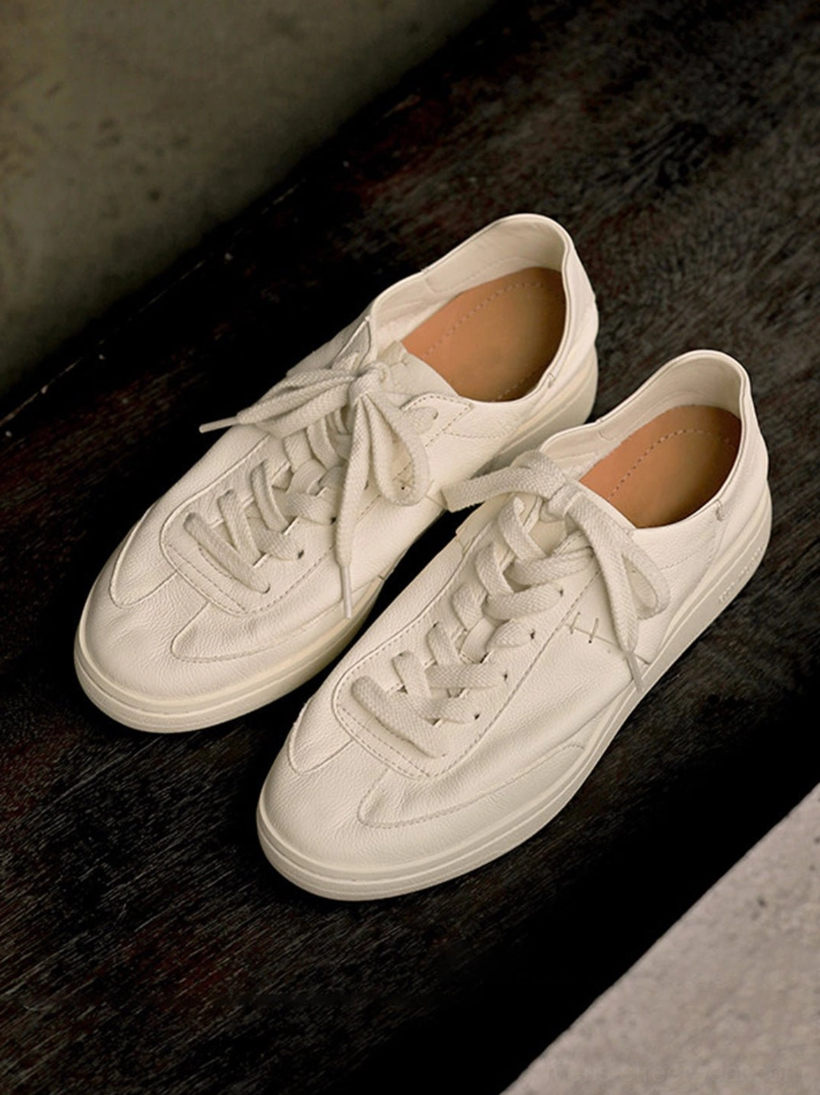 Off-white low-profile leather sneakers arranged on a dark wood surface, showing the classic retro tennis shape and rubber outsole