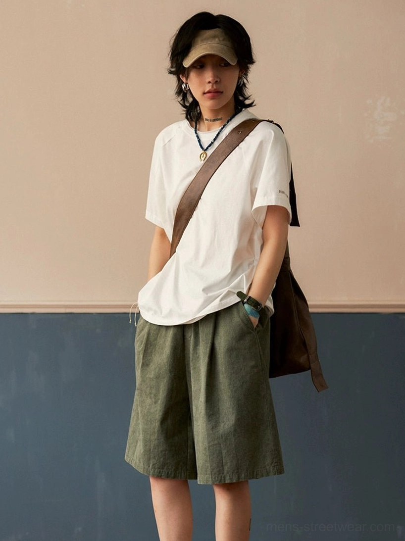 Off-white oversized cotton raglan crew neck T-shirt styled with green wide-leg shorts and canvas crossbody bag