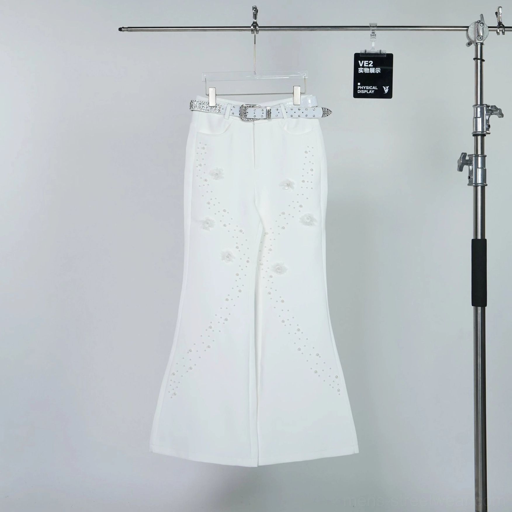 Hanging view of off-white pearl and floral embellished wide flare trousers with matching rhinestone-style belt on clothing rack
