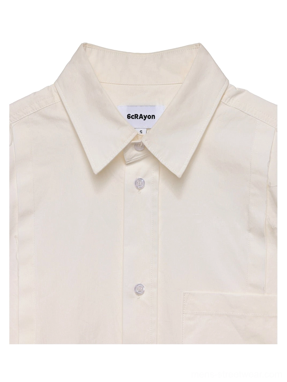 Close-up of subtle black embroidered monogram on curved hem of off-white cotton poplin streetwear overshirt