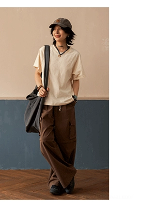 Off-white relaxed cotton raglan T-shirt with brown cargo pants, canvas shoulder bag, and newsboy cap