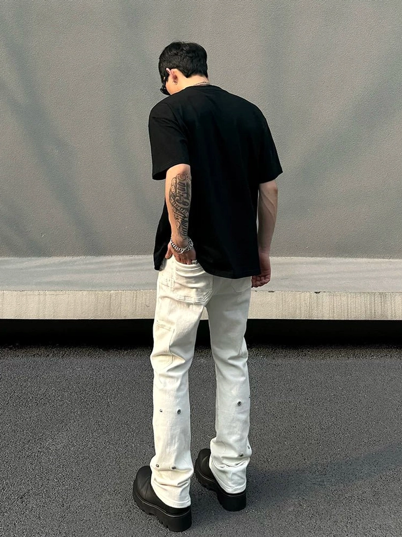 Rear full-body view of men's off-white snap-hem utility flare jeans with back pockets and metal stud details along outer legs