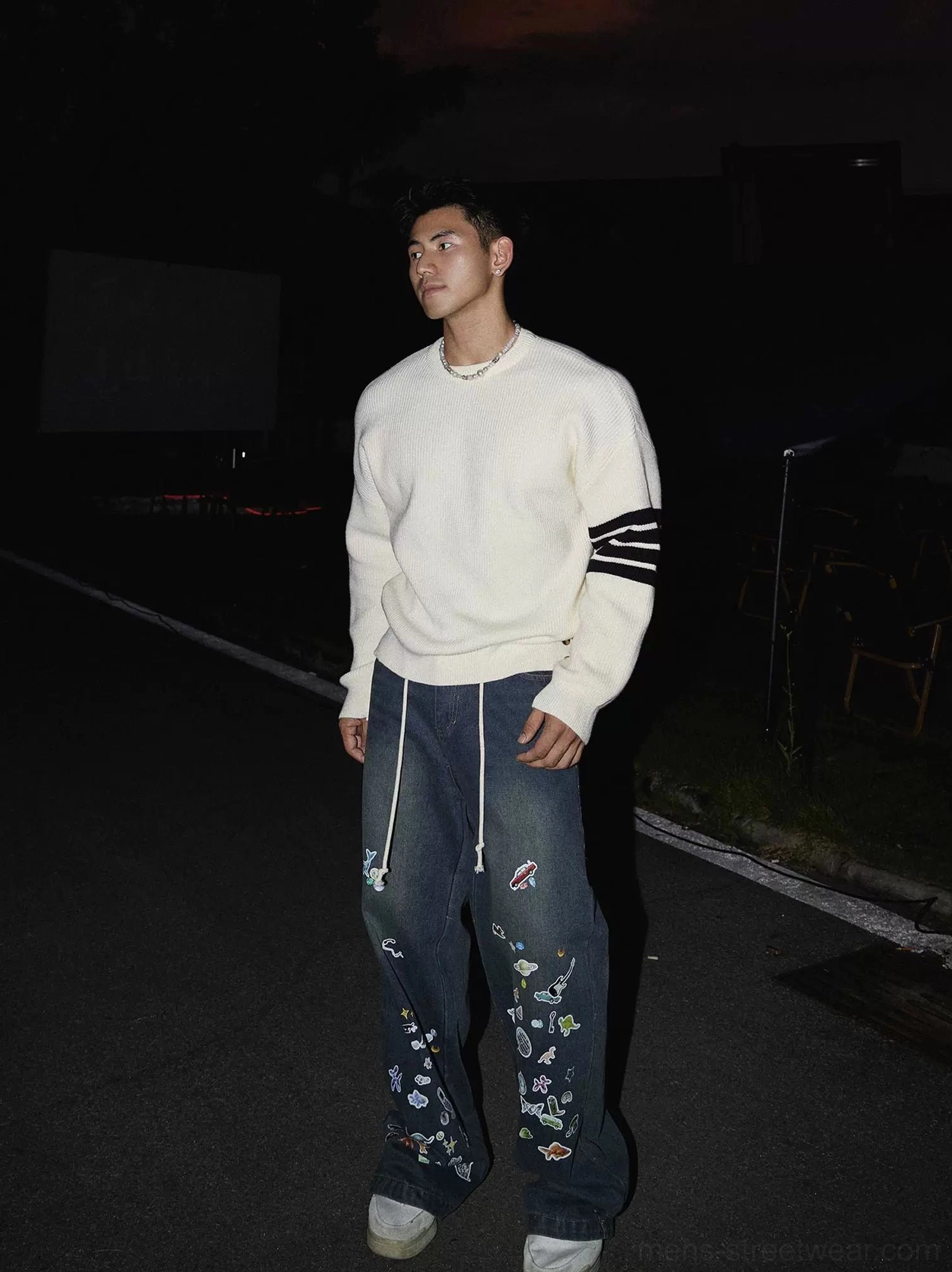 Side view of an off-white Korean streetwear crewneck sweater with black striped sleeve trims, long loose sleeves, drop shoulders, and metal hem buttons