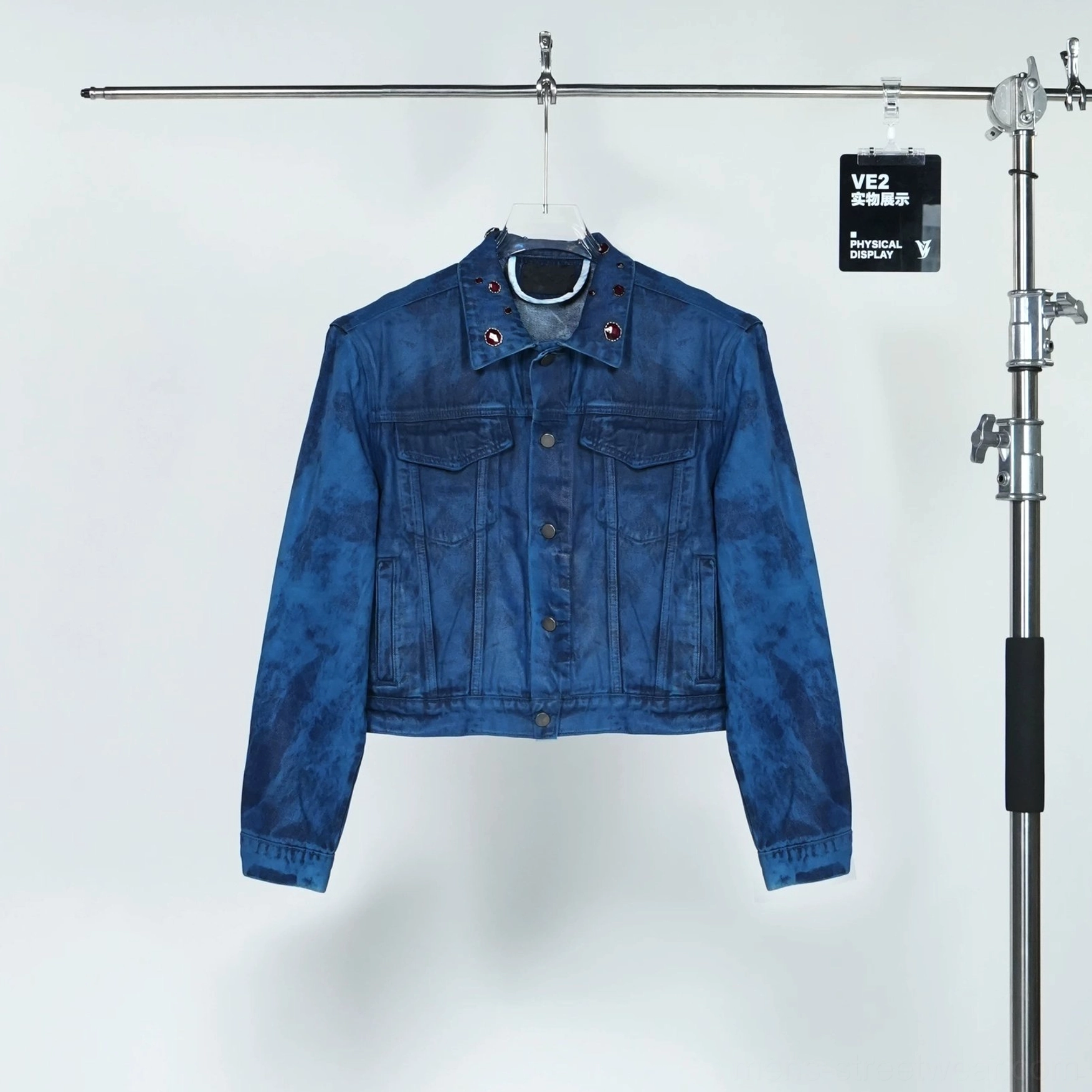 Oil wax blue cropped denim jacket hanging on studio rack with marbled indigo wash, metal collar grommets, buttons, and chest pockets