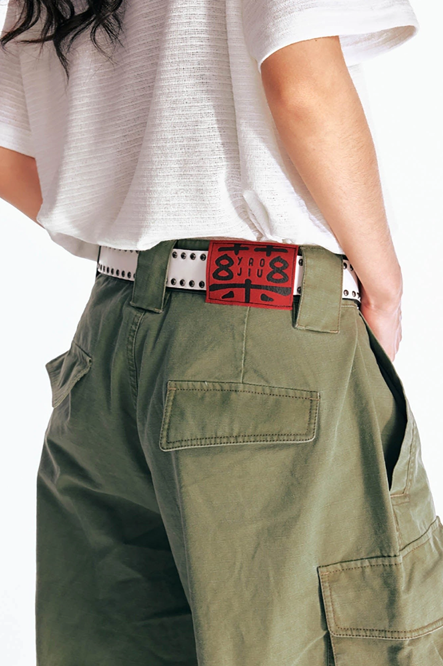 Close up of olive green cargo Bermuda shorts rear waist and patch pockets with detailed stitching, perforated belt, and utility streetwear construction