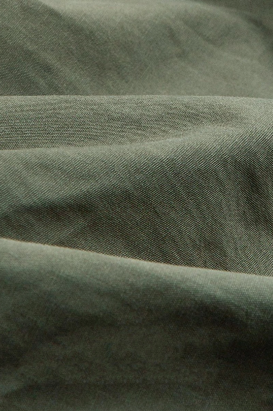 Close-up view of woven cotton fabric texture on olive green utility cargo pants with natural folded creases
