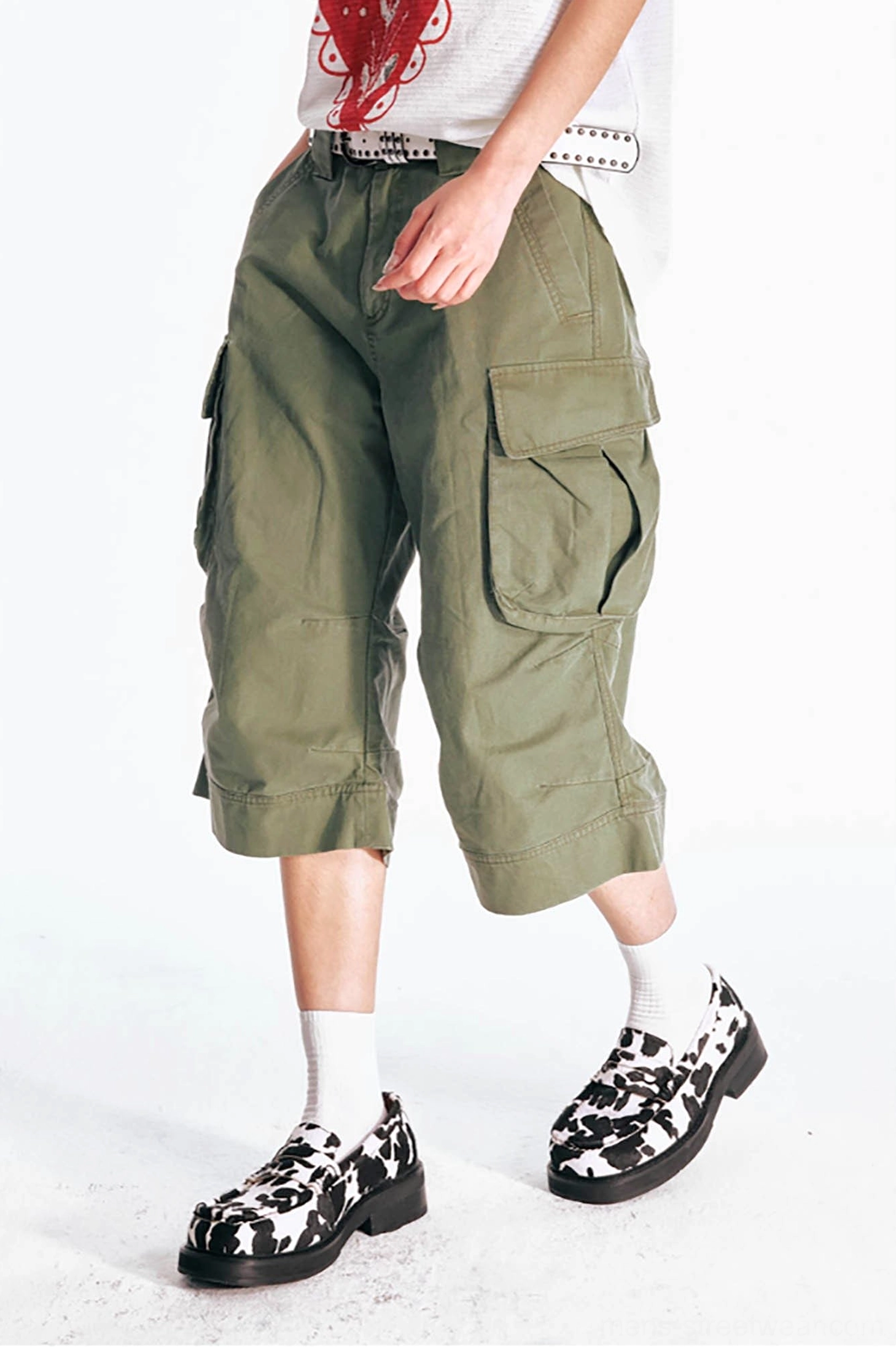 Side angle detail of olive green flared cargo Bermuda shorts showing relaxed waist fit, oversized utility pocket, faded cotton canvas texture, and wide leg