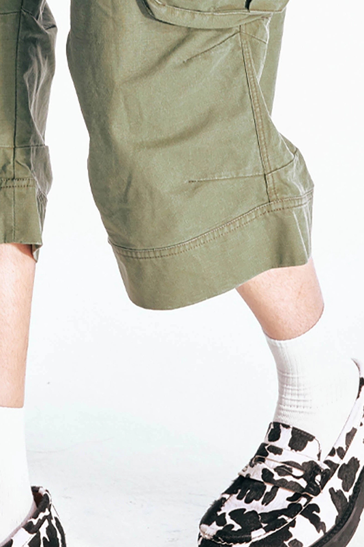 Low angle close up of olive green flared cargo Bermuda shorts wide stitched hem with loose drape, white socks, platform loafers, and cotton twill texture