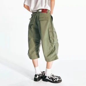 Back view of olive green oversized flared cargo Bermuda shorts showing rear patch pocket, relaxed streetwear silhouette, white T-shirt, belt, socks, and platform loafers