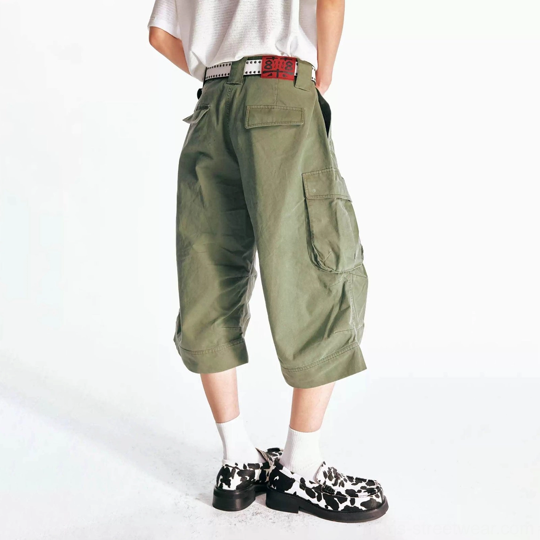Back view of olive green oversized flared cargo Bermuda shorts showing rear patch pocket, relaxed streetwear silhouette, white T-shirt, belt, socks, and platform loafers