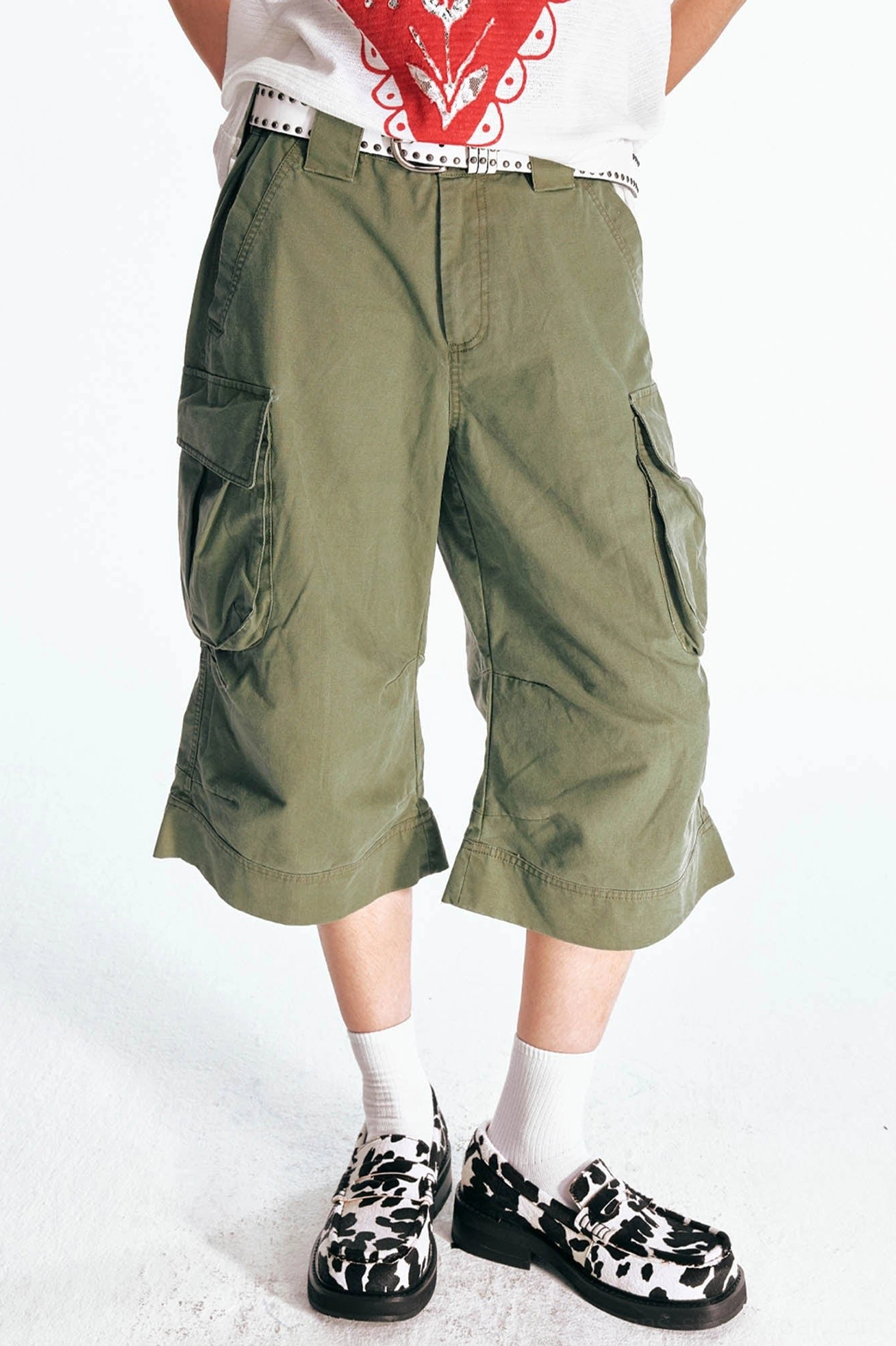 Three quarter front view of olive green streetwear cargo Bermuda shorts with oversized side pocket, wide stitched hem, and relaxed flared cropped fit