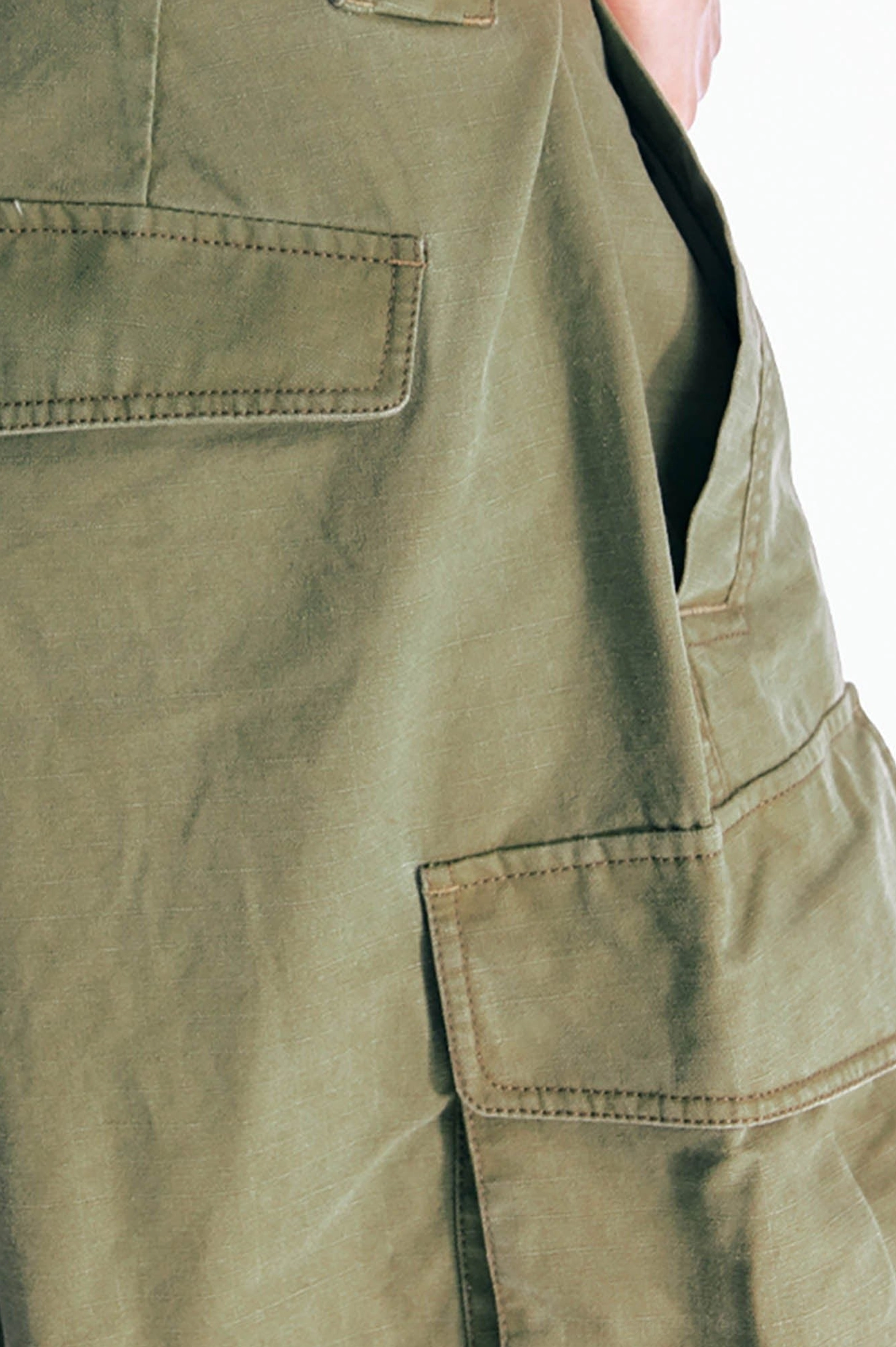 Close up of olive green utility cargo shorts layered patch pockets with precise topstitching and structured army green cotton twill fabric