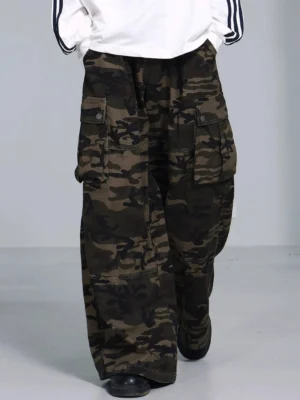 Olive green woodland camouflage wide leg cargo pants shown from a low front three quarter angle with oversized loose legs and flap cargo pockets