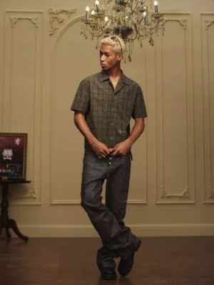 Front view of a relaxed olive plaid camp collar shirt with sparkling embellishments styled with wide-leg dark trousers