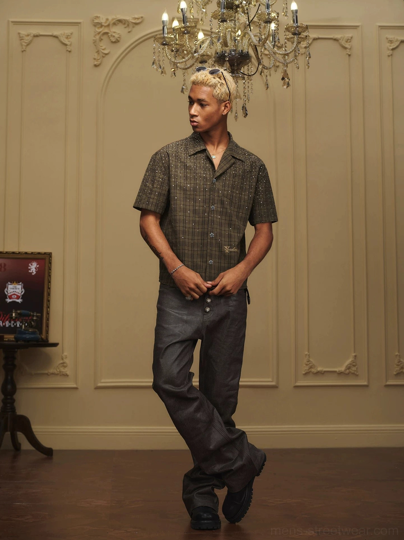 Front view of a relaxed olive plaid camp collar shirt with sparkling embellishments styled with wide-leg dark trousers