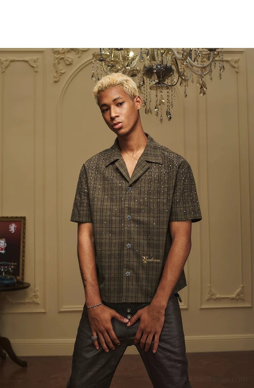 Front streetwear styling of a relaxed olive plaid short sleeve camp collar shirt with dark trousers