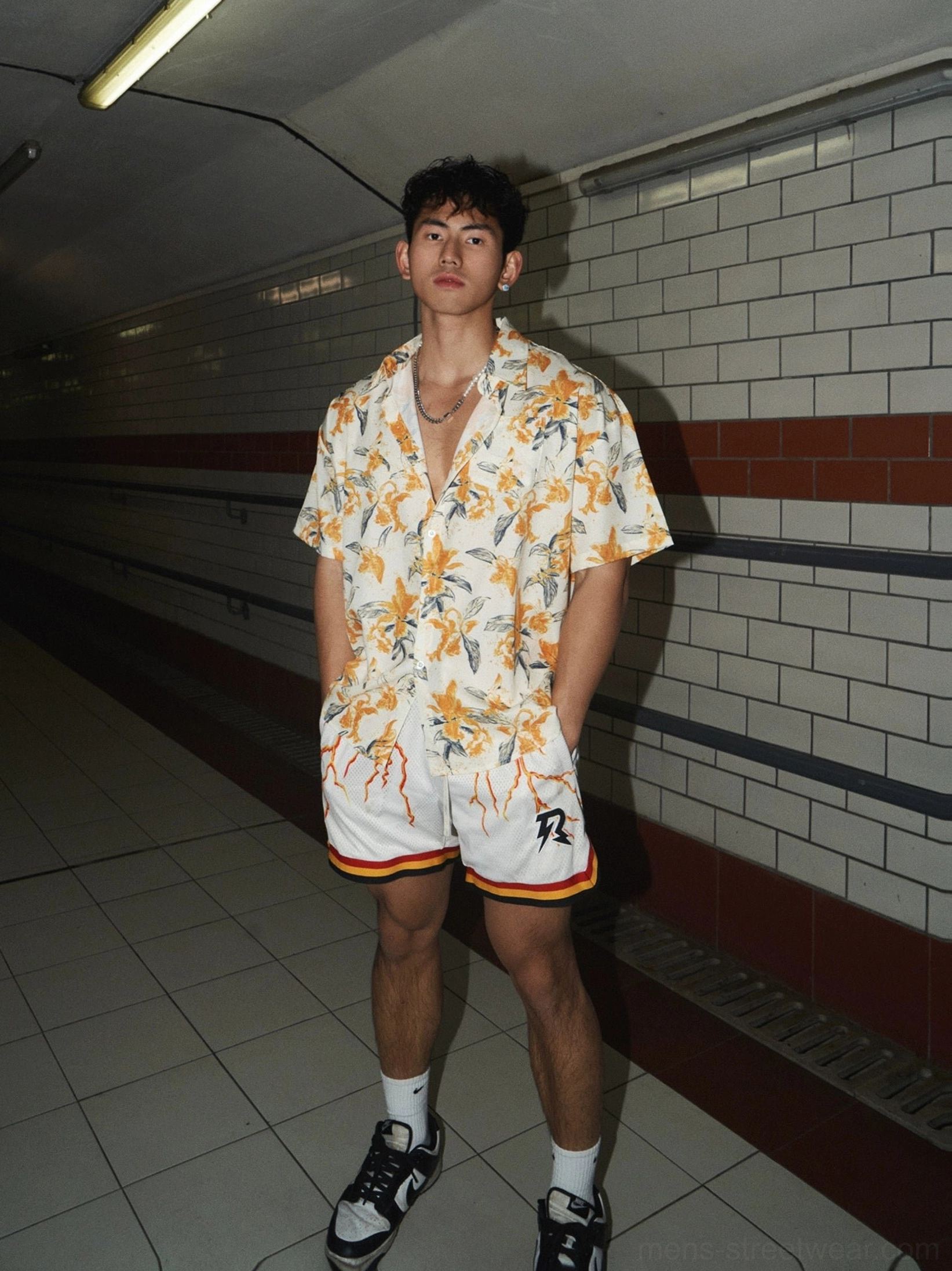 Front view of a relaxed orange and cream floral short sleeve shirt styled with coordinated athletic shorts, socks, and skate shoes