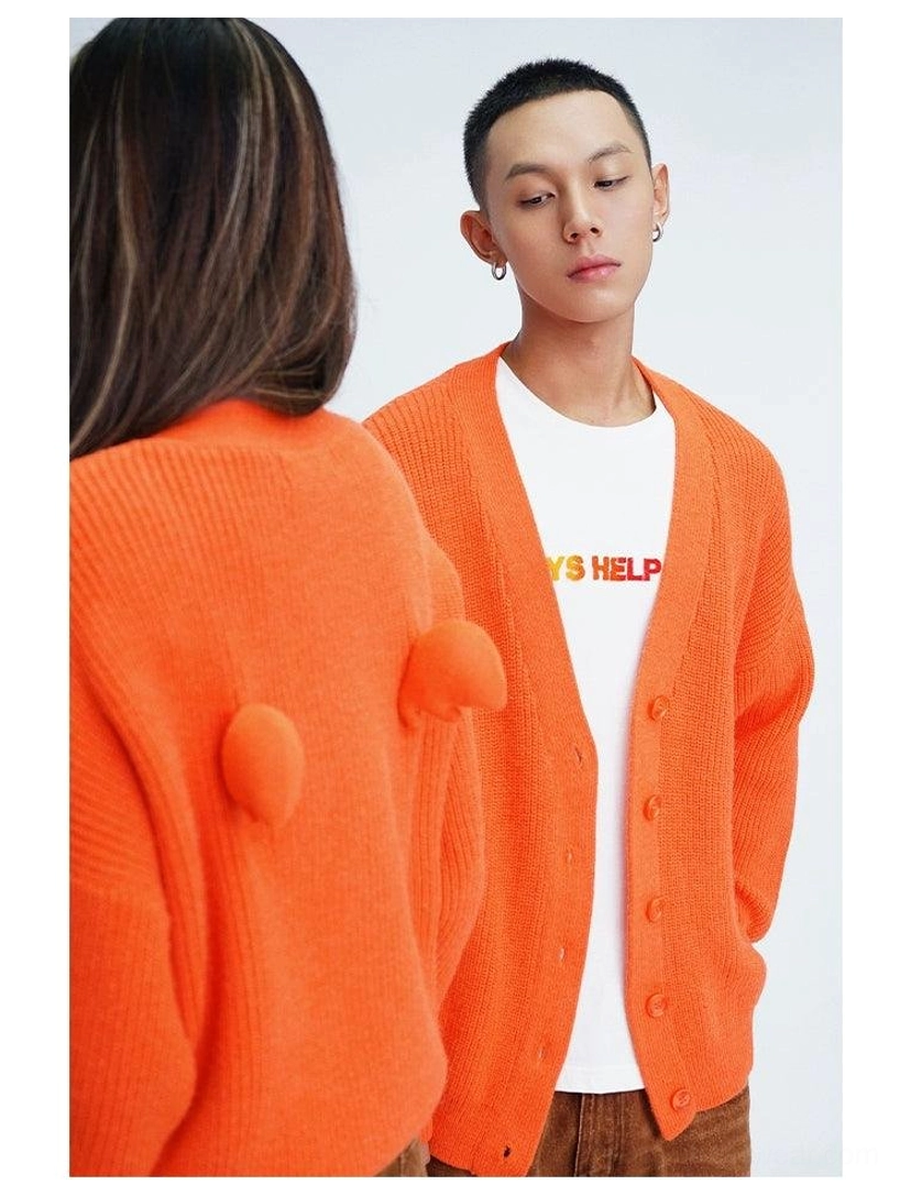 Orange oversized fuzzy cardigan shown on two models with button-down V-neck front, ribbed knit texture, and playful pom-pom back decorations