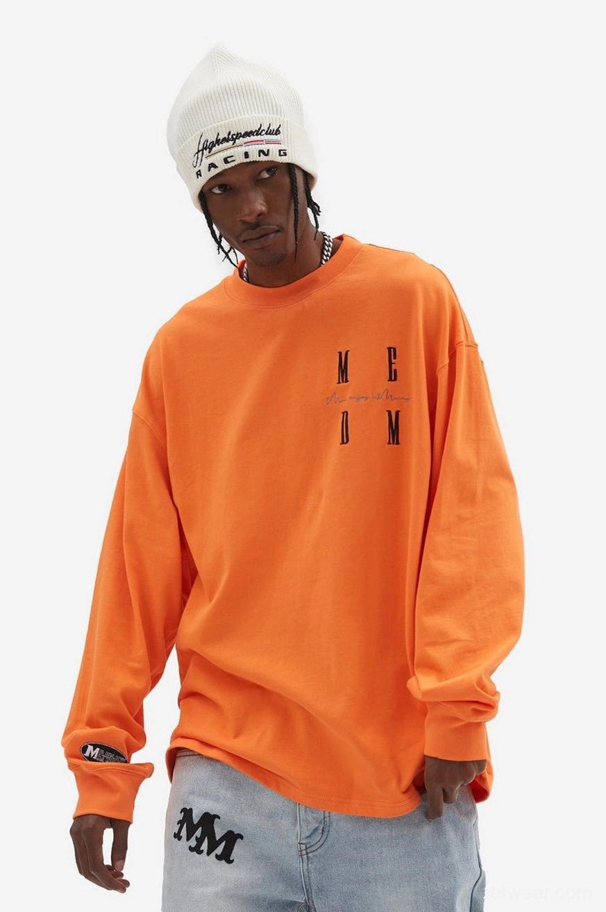 Bright orange oversized graphic long sleeve T-shirt with chest lettering and cuff tag styled with printed jeans