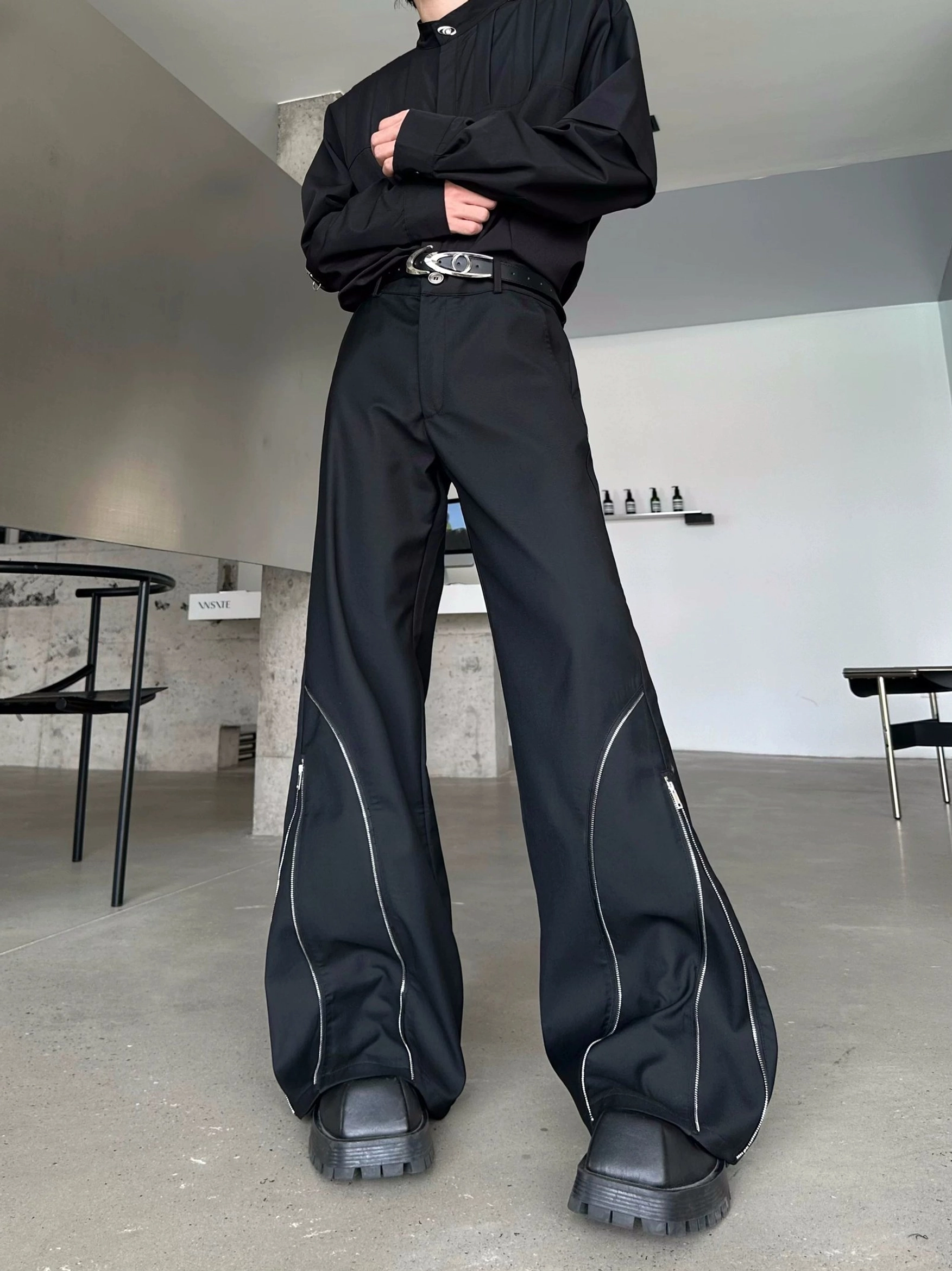 Black Orbit Sculpt streetwear trousers shown from the front with prominent silver side zippers, oversized wide-leg shape, and grey-soled platform shoes