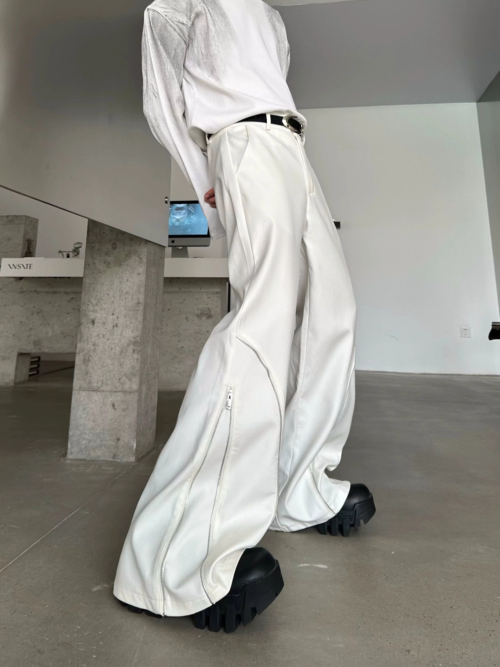 Off-white Orbit Sculpt wide-leg trousers shown from a low-angle back three-quarter view with curved leg seams, outer zipper details, and extra-long draped length