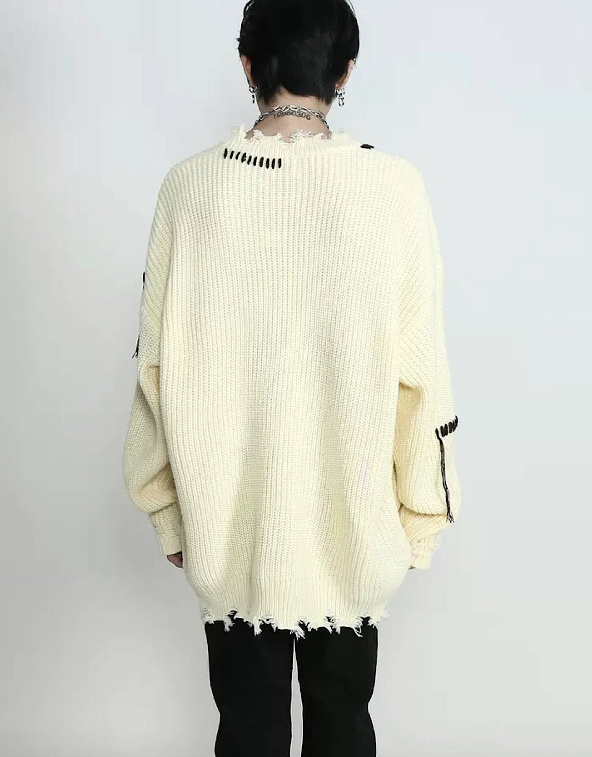 Back view of an oversized apricot ribbed knit sweater featuring black whipstitch sleeve accents, drop shoulders, and an uneven frayed hem