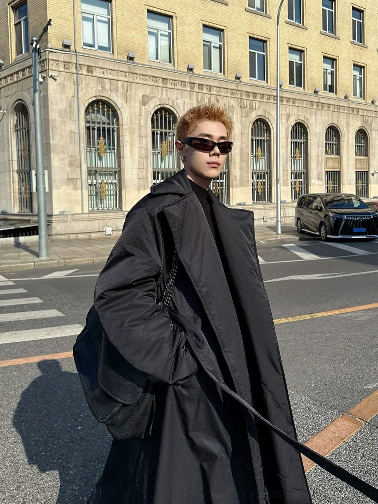 Front three quarter view of an oversized black belted padded overcoat with ankle length cut wide lapels and dropped shoulders styled as Seoul streetwear