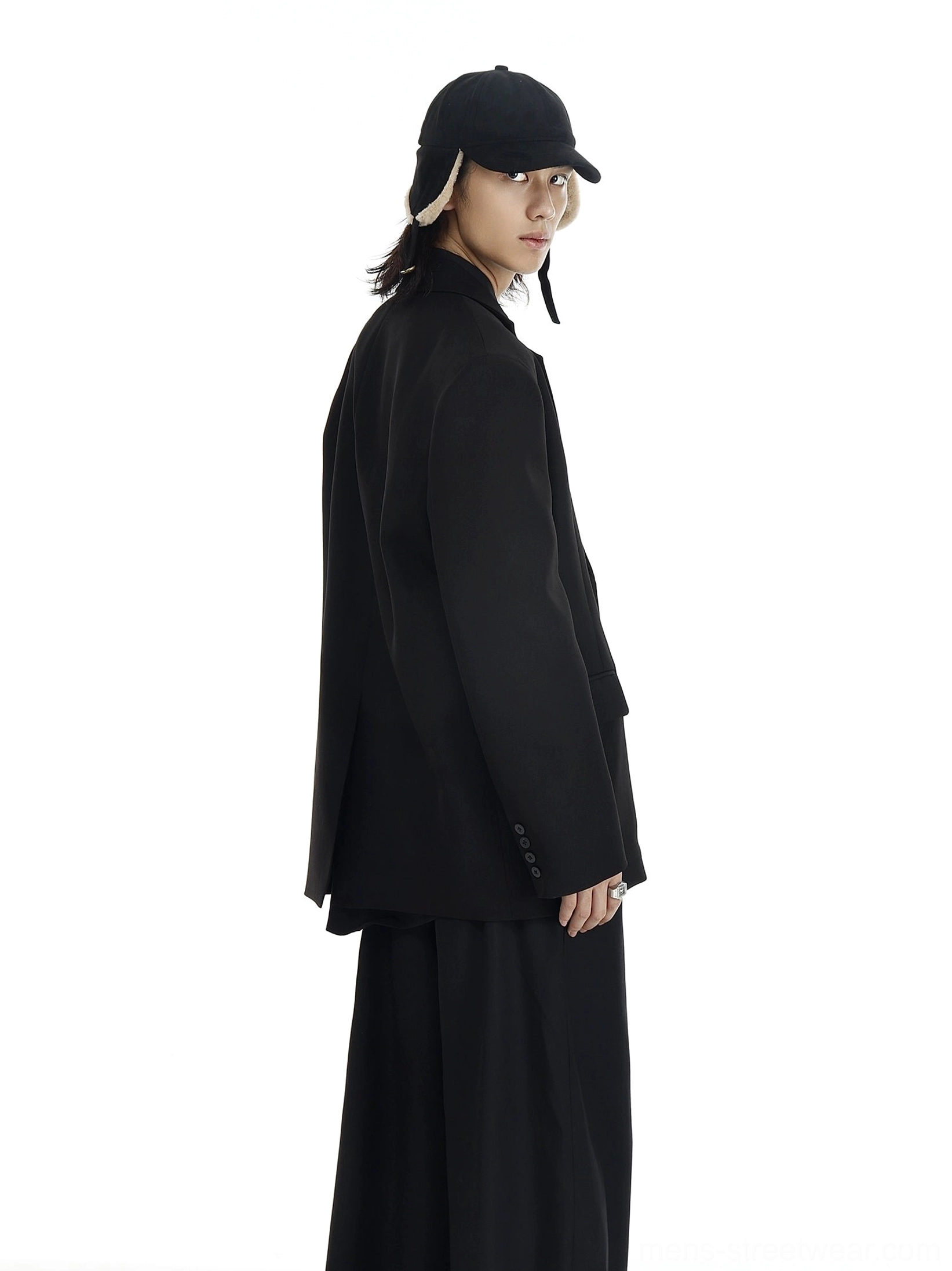 Oversized black blazer shown in side profile with flowing skirt-style wide-leg trousers and earflap cap