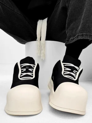 Oversized black and cream platform sneakers with rounded toe, white contrast laces, chunky rubber sole, and streetwear styling worn with black jeans
