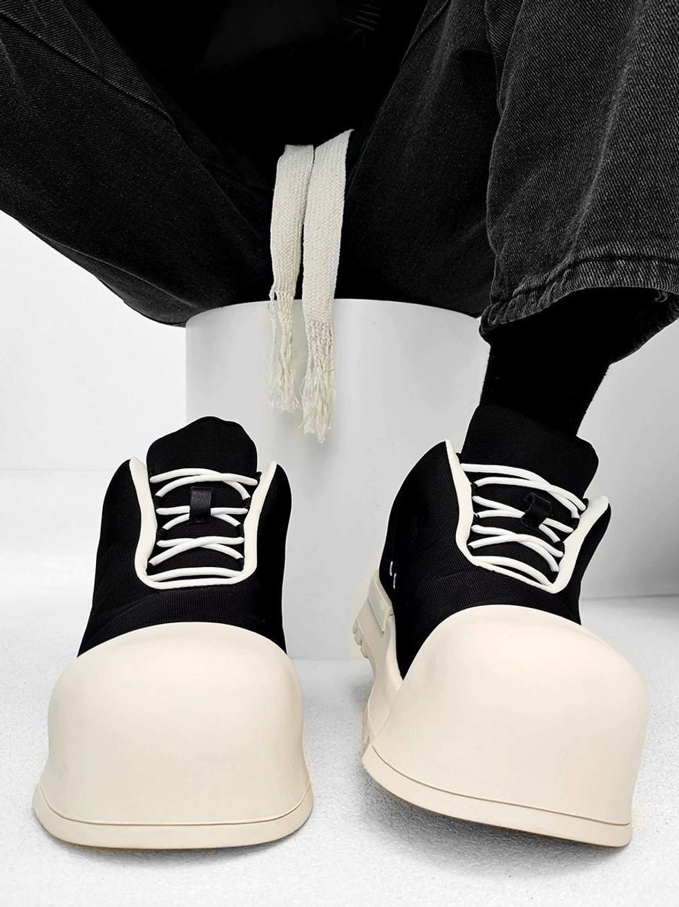 Oversized black and cream platform sneakers with rounded toe, white contrast laces, chunky rubber sole, and streetwear styling worn with black jeans