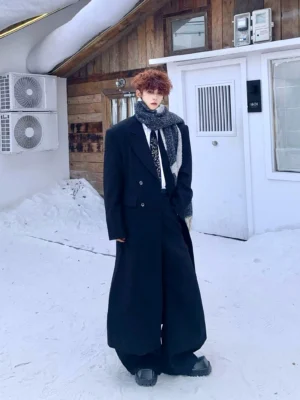 Oversized black double-breasted floor-length overcoat styled with a fringed scarf in a snowy cabin setting