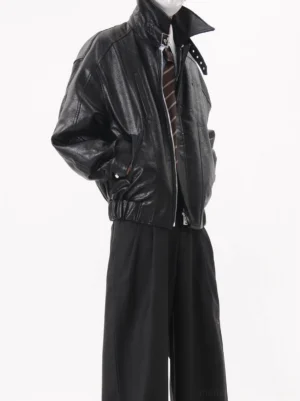 Black oversized faux leather buckle collar zip-up bomber jacket shown in left three-quarter view with shirt tie and wide-leg trousers