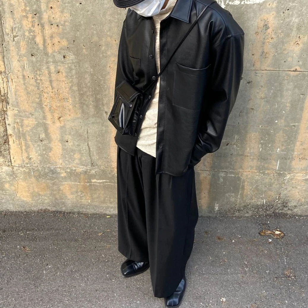 Three quarter view of oversized black faux leather shirt jacket with button placket, long sleeves and urban crossbody styling
