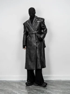 Three quarter side view of long black faux leather trench coat styled with wide leg pants and chunky black sneakers