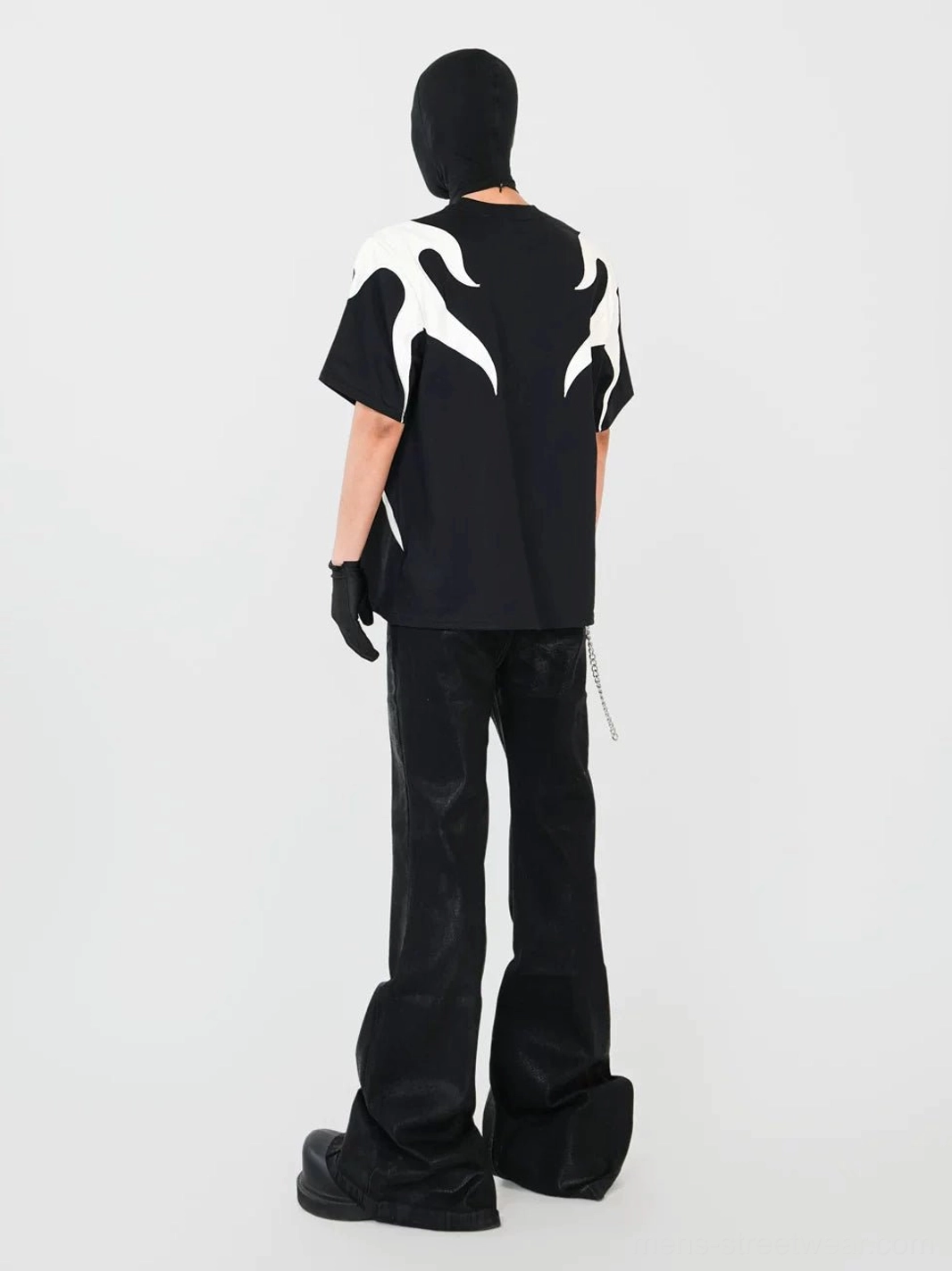 Full back view of a relaxed oversized black flame appliqué T-shirt displaying the complete off-white rear design with wide-leg leather pants and dark streetwear accessories