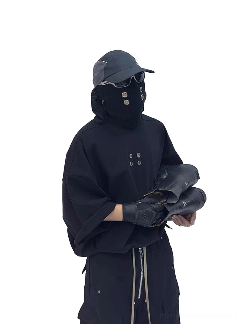 Three-quarter view of oversized black grommet T-shirt styled with black cargo pants in a techwear outfit