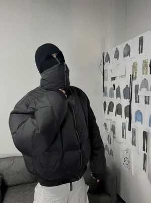Model wearing an oversized black high-collar down puffer jacket with white loose pants in a contemporary streetwear studio setting