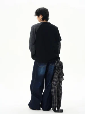 Back view of an oversized layered varsity long sleeve tee in black with contrast striped sleeves styled with wide leg denim streetwear pants