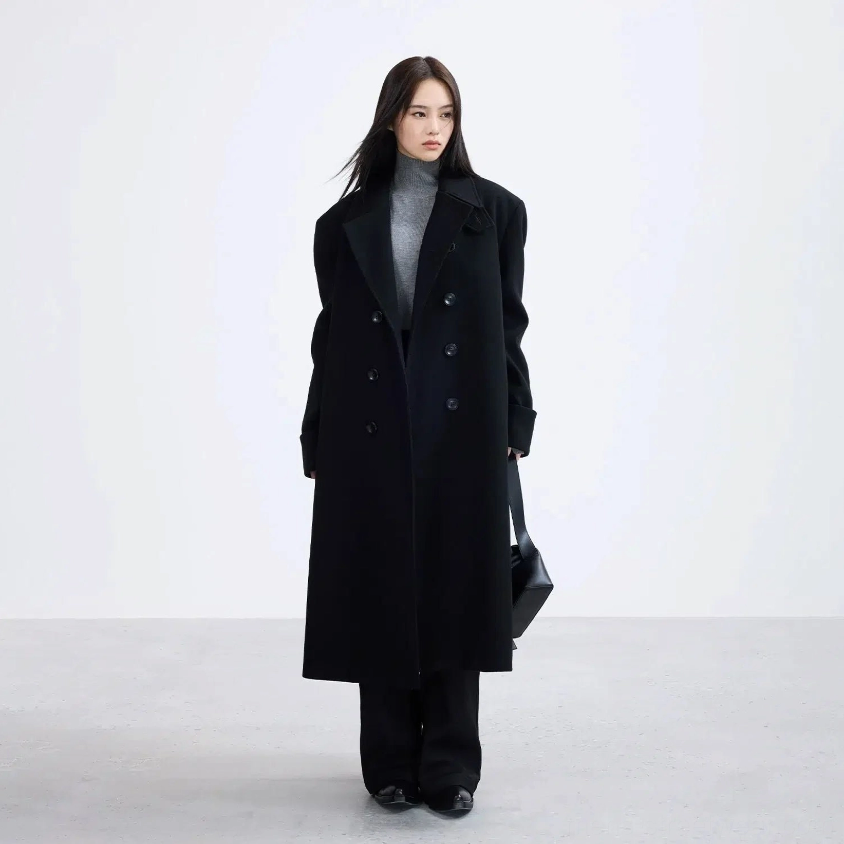 Full body styling view of oversized black long overcoat layered over a grey turtleneck in minimalist Seoul fashion style