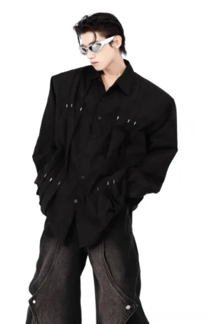 Model wearing an oversized black metal rivet shirt with vertical pleats, silver hardware, wide-leg denim, and futuristic streetwear sunglasses