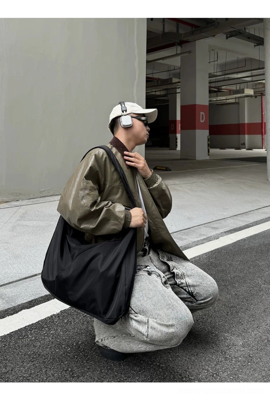 Oversized black nylon crossbody sling bag worn comfortably across the torso in an indoor parking setting